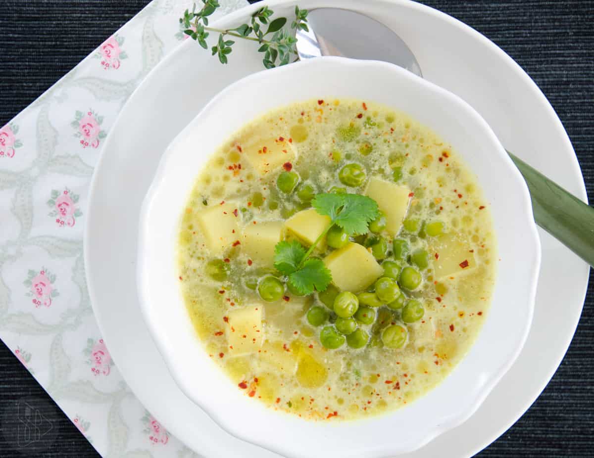 Zupa w białej miseczce dużą ilością zielonego groszku, ziemniaków posypana płatkami chilli.