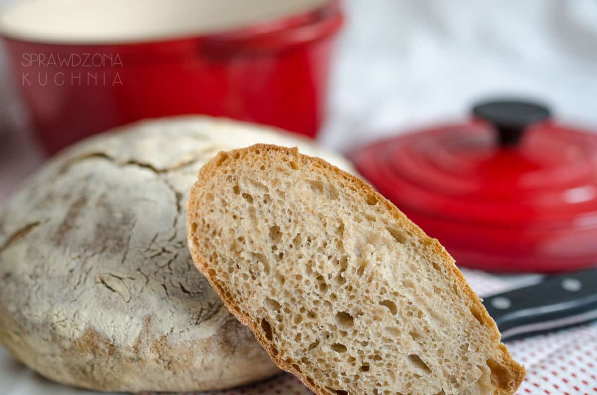 Ukrojona kromka chleba położona na bochenku w tle garnek żeliwny do pieczenia chleba.