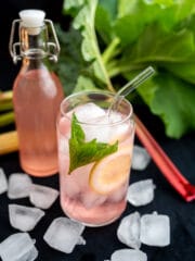 różowa lemoniad rabarbarowa w szklance pełnej lodu z cytryną i miętą w tle butelka z lemoniadą