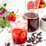szklanka z czerwonym napojem z hibiskusa w tle kwiaty i butelka z napojem