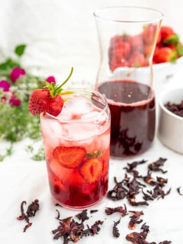 szklanka z czerwonym napojem z hibiskusa w tle kwiaty i butelka z napojem