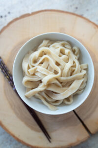 ugotowany makaron udon w miseczce obok pałeczki