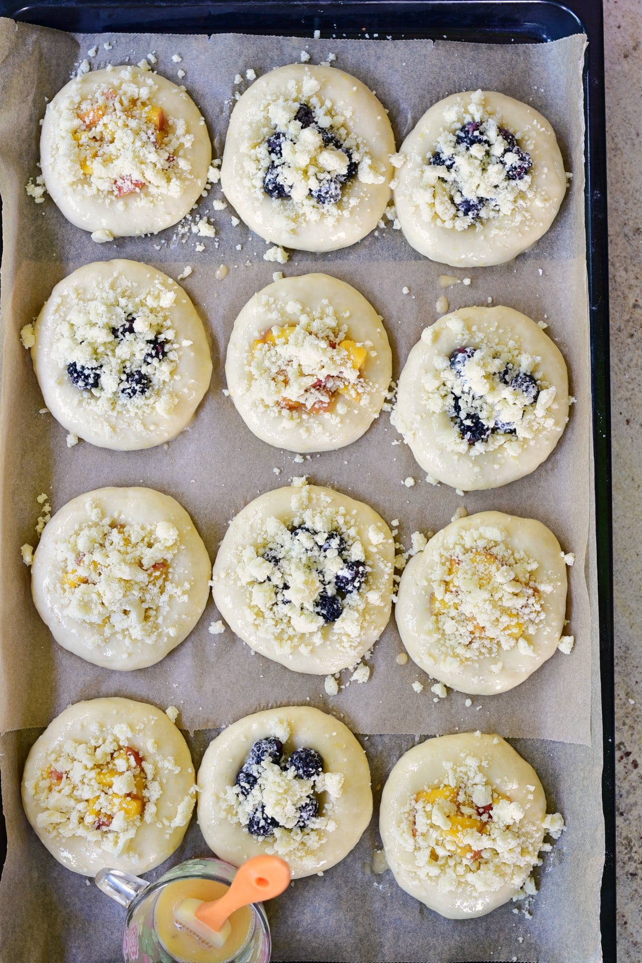 wyrośnięte bułki drożdżowe z owocami na blaszce do pieczenia