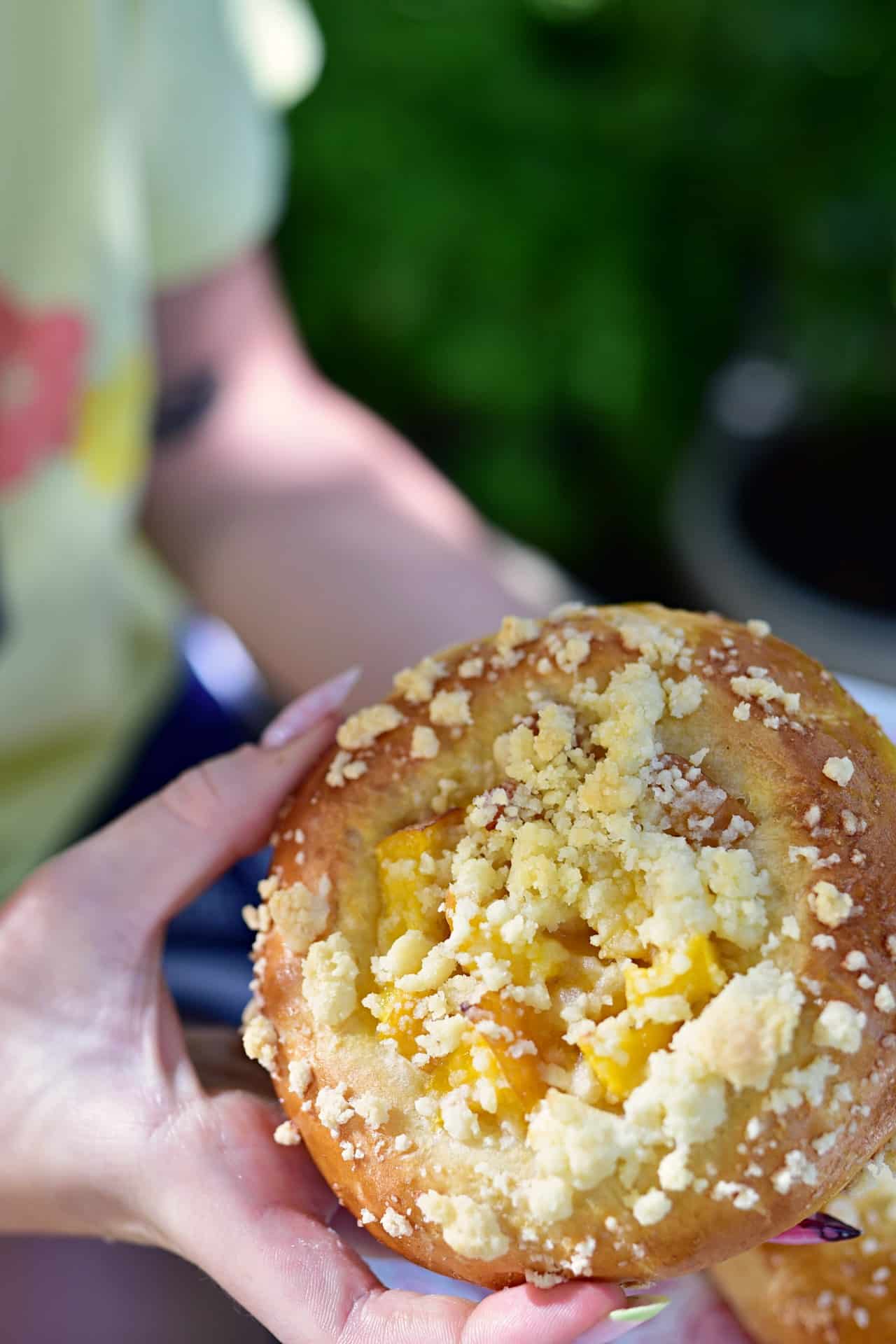 rumiana drożdżówka z brzoskwinią i kruszonką trzymana w ręku dziewczyny